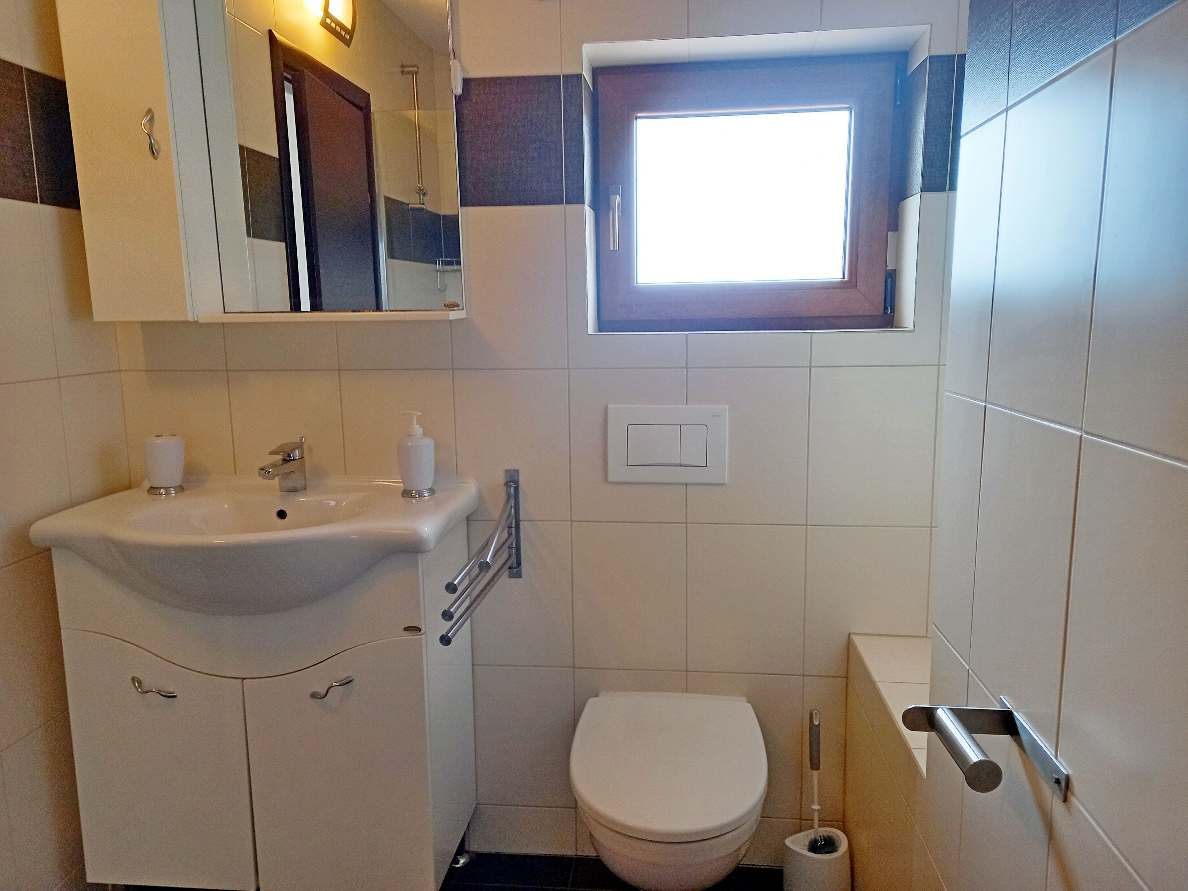 Ein kleines Badezimmer mit Waschbecken, Toilette und Fenster.