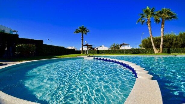 A swimming pool with a clear blue water, surrounded by palm trees and a well-maintained lawn. - Premium Holiday House  (Torrevieja)
