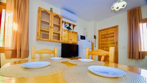 A dining area with a wooden table, four chairs, and a television. There are cabinets above the table and a door to the right. - Premium Holiday House  (Torrevieja)