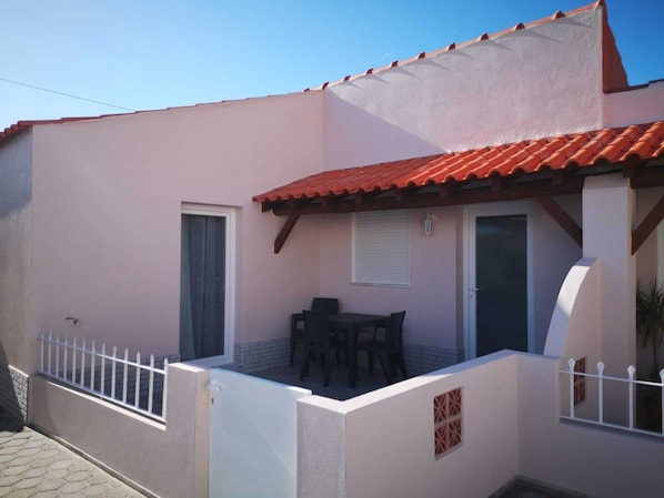 A single-story building with a red-tiled roof, a small patio with a table and chairs, and a white fence.