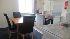 A compact kitchen with a dining table, chairs, a microwave, a small oven, and a sink. - Lennard House (Folkestone)