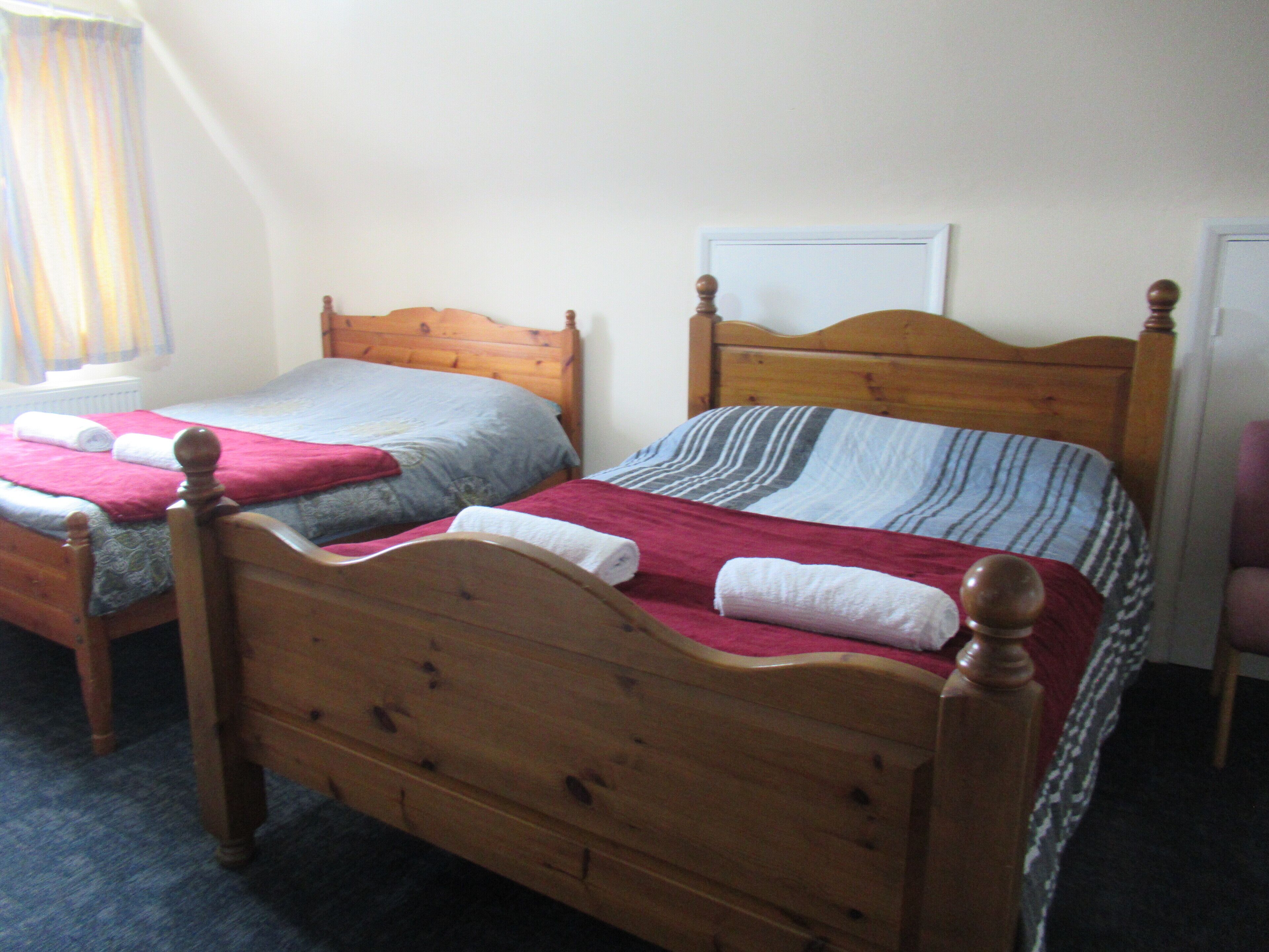 Two wooden beds with headboards, a window with curtains, and a door in a room.