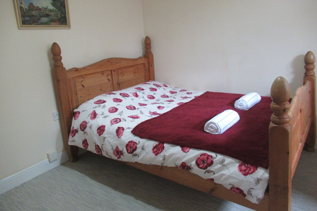 Uma cama de solteiro com colcha floral, um cobertor vermelho e duas toalhas enroladas.