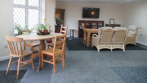A dining area with a round table and chairs, a bookshelf, a television, and wicker furniture. - Lennard House (Folkestone)