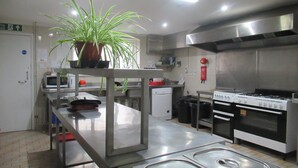 A commercial kitchen with stainless steel appliances, a potted plant, and a fire extinguisher. - Lennard House (Folkestone)