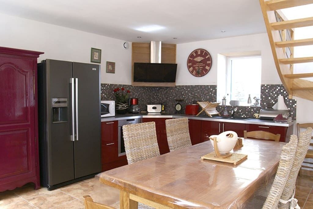 A modern kitchen with a built-in refrigerator, microwave, and stove. There is a dining table with chairs and a clock on the wall.