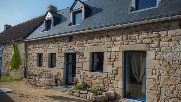 A stone building with a sloped roof, a small porch with a table and chairs, and a window with a curtain. - La plage à pied - Plouhinec (Plouhinec)