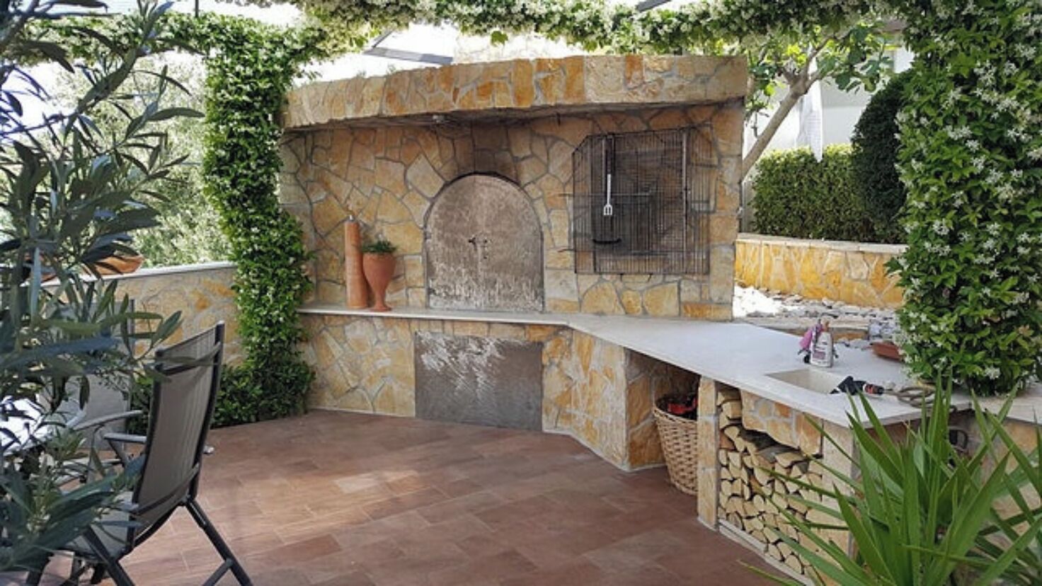 An outdoor kitchen area with a stone wall, a built-in oven, and a sink.
