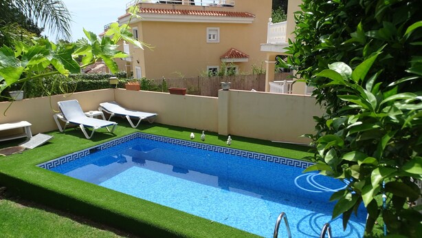 A rectangular swimming pool with a blue interior and a decorative edge, surrounded by artificial green grass and white lounge chairs. - Torremolinos in el Pinar LONG TERM RENT INDEPENDENT house with pool  (Torremolinos)