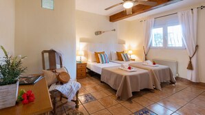 Una camera d'albergo accogliente con due letti, una ventola a soffitto, una finestra con tende e un tavolino con una pianta e un cappello.