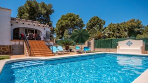 Una piscina con lettini e un ombrellone, circondata da un edificio con scale e vista sugli alberi.