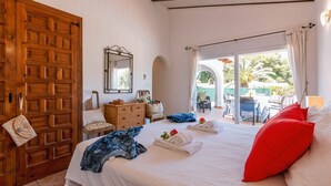 Una camera da letto con un letto grande, una porta in legno, un comò, uno specchio e vista su un patio esterno con tavoli e sedie.