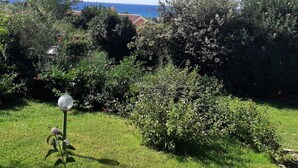 Un jardin avec un lampadaire, différents arbustes et une vue sur la mer et les bâtiments au loin.