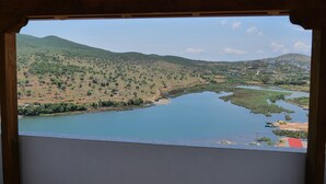 A view from a wooden-framed window overlooking a valley with a lake, hills, and distant buildings. - Pellumb Apartments (Ksamil)