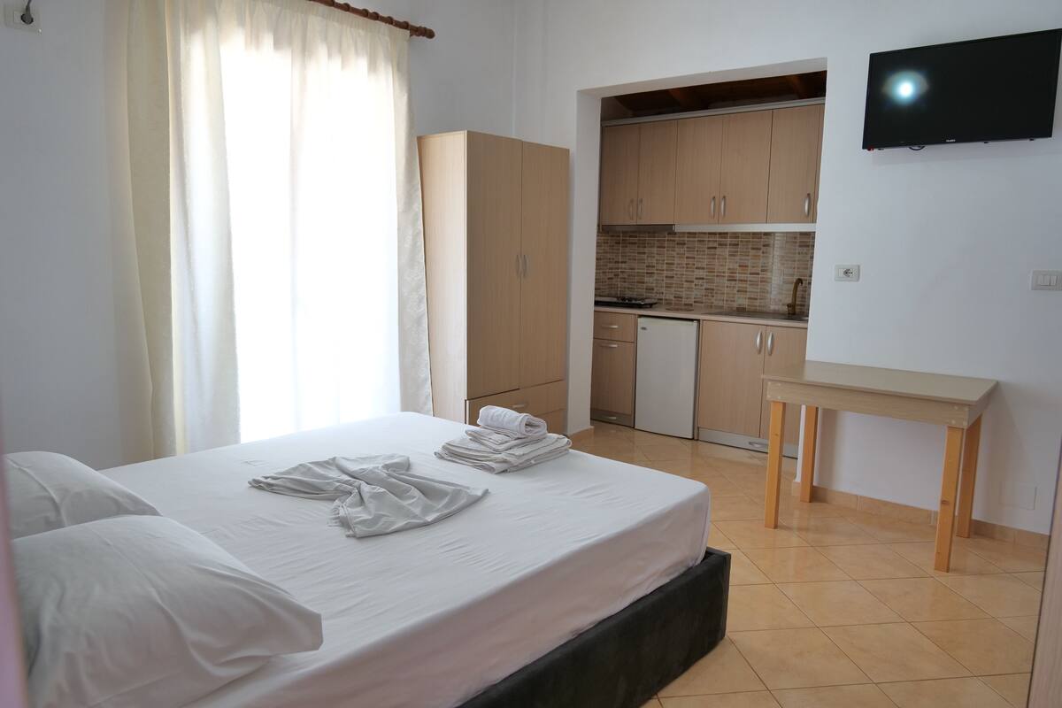 Una habitación de hotel con cama, escritorio, kitchenette y televisión.