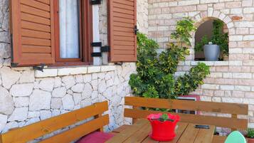 A stone wall with wooden shutters, a wooden table with benches, and potted plants.