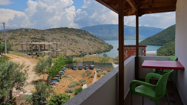 A balcony with a view of a lake, a building under construction, and green chairs. - Pellumb Apartments (Ksamil)