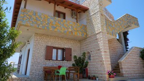 A two-story stone house with a balcony, a wooden table, and chairs outside. - Pellumb Apartments (Ksamil)