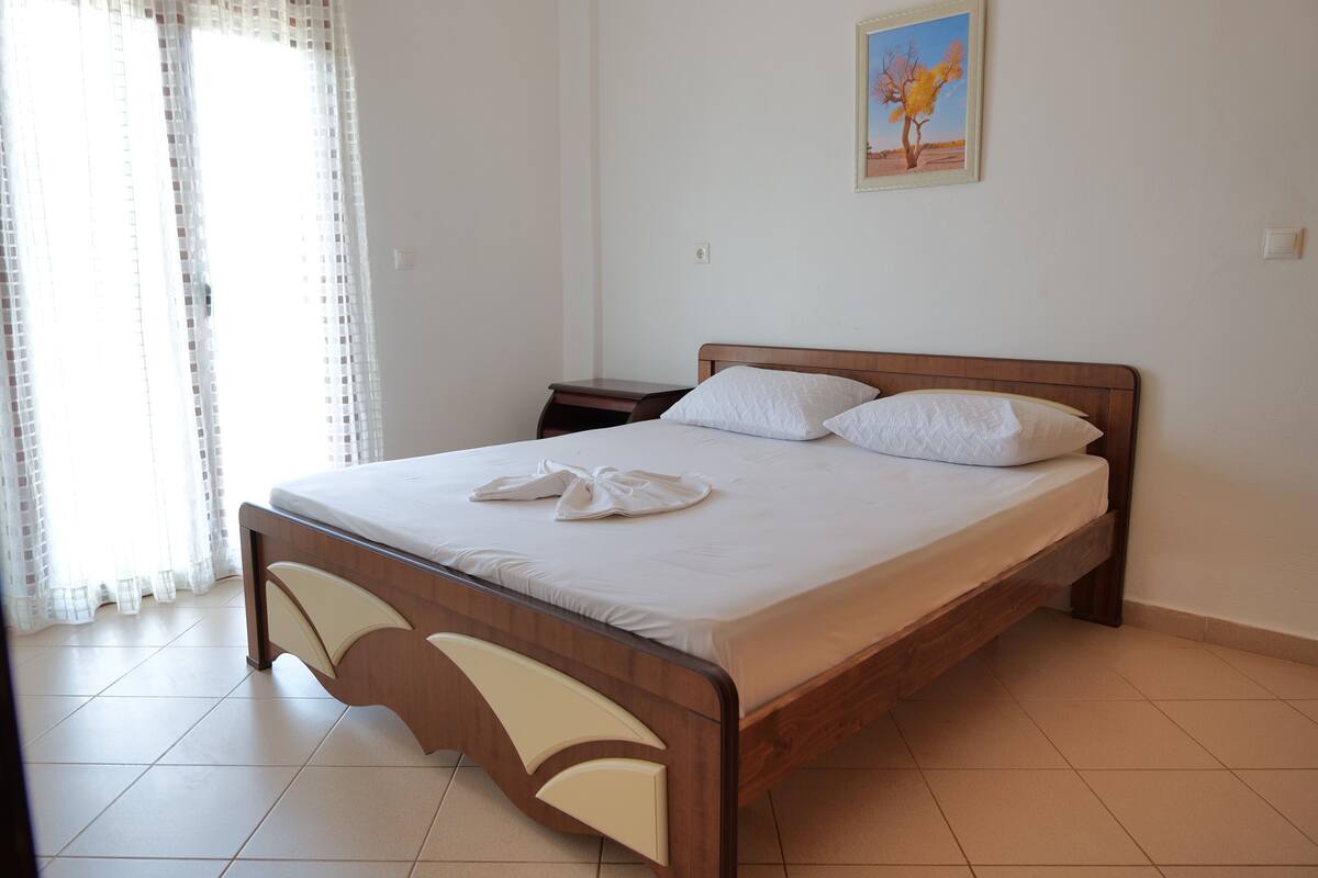 Una cama bien hecha con sábanas blancas y dos almohadas, un cabecero de madera, una mesita de noche y un cuadro en la pared.