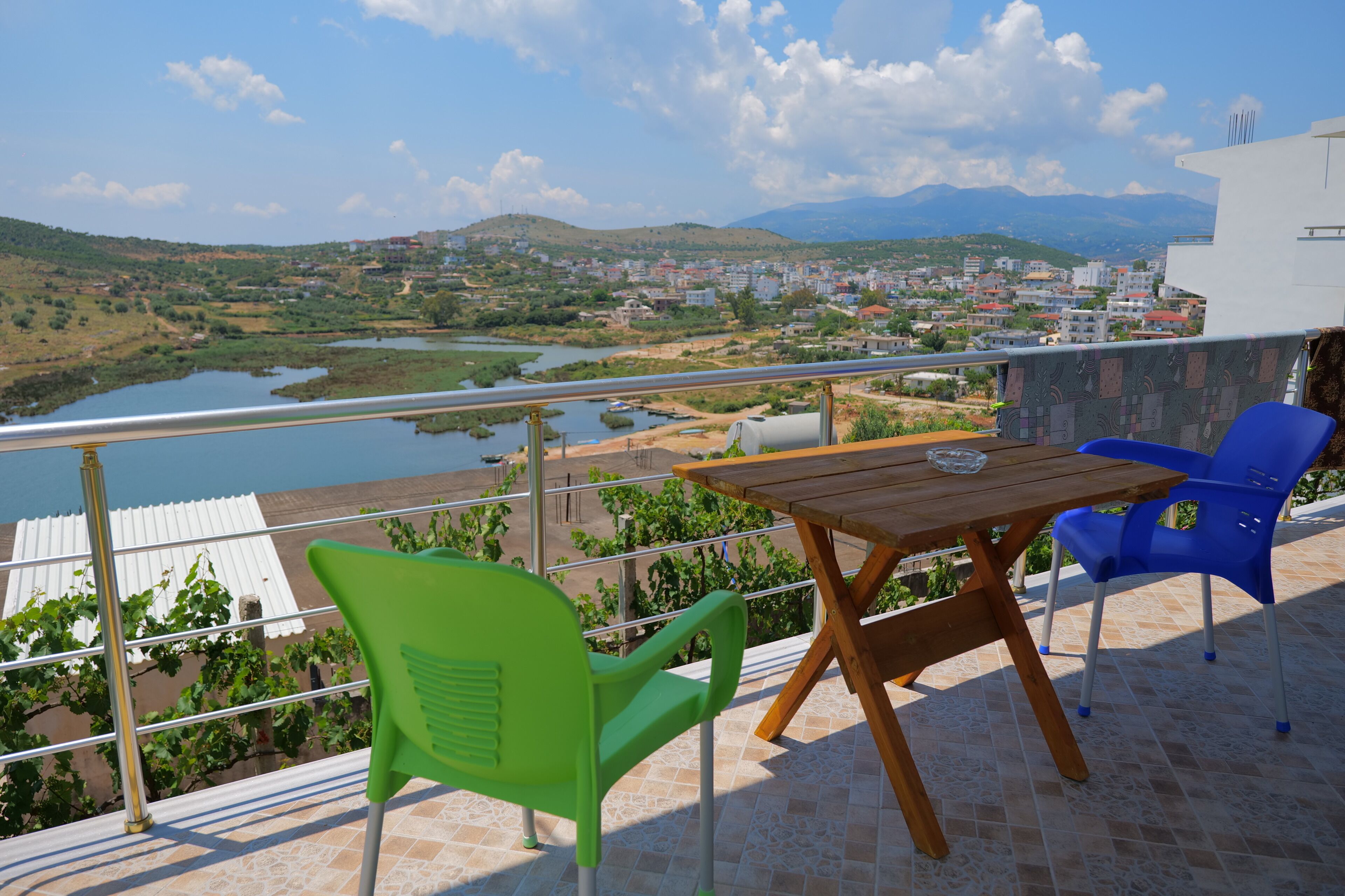 Una terraza con una mesa de madera y dos sillas, con vistas a un paisaje pintoresco que incluye un río y edificios.