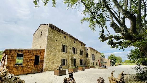 Ein rustikales Steinhaus mit Innenhof, umgeben von Bäumen und Holzskulpturen.