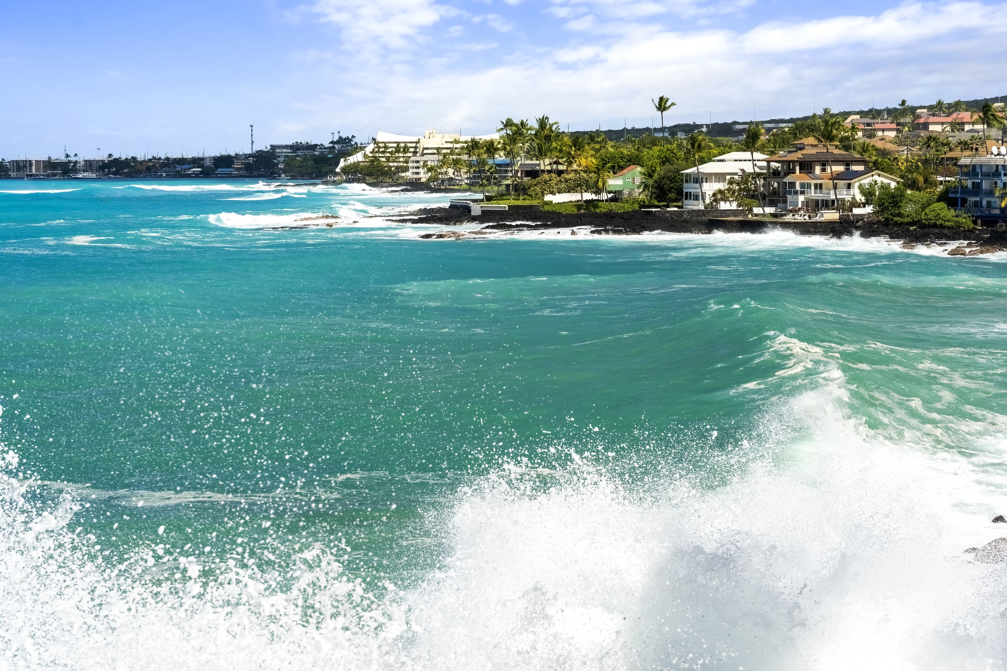 A coastal view with clear turquoise waters, a rocky shoreline, and residential buildings with balconies overlooking the sea.