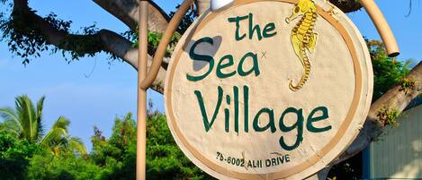 Une pancarte en bois portant l’inscription « The Sea Village » et illustrée d’un hippocampe, fixée à un arbre.
