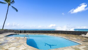 Uma piscina com deck de pedra, uma palmeira e vista para o oceano.