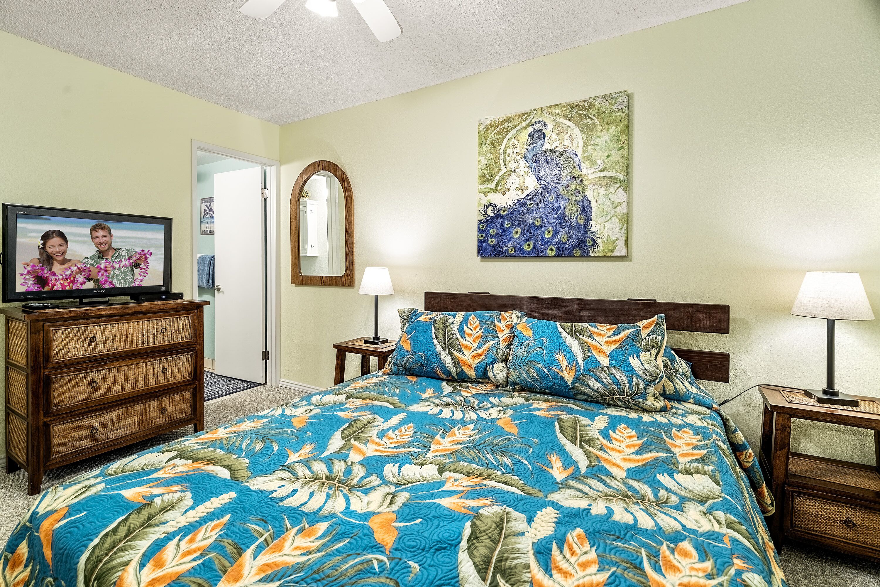 A bedroom with a bed, a television on a dresser, a painting on the wall, and two bedside lamps.