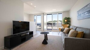 A modern living room with a flat-screen TV, a sofa, a coffee table, and a balcony with a view. - La Concha Terrace - The Rentals Collection (San Sebastián)