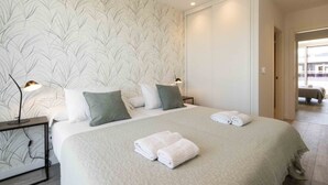 A hotel room with a large bed, two bedside lamps, a nightstand, and a view of the outside. - La Concha Terrace - The Rentals Collection (San Sebastián)