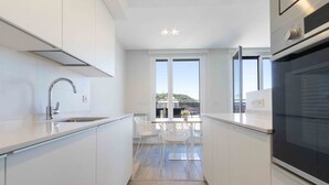 A modern kitchen with white cabinetry, a stainless steel sink, and a built-in oven. - La Concha Terrace - The Rentals Collection (San Sebastián)