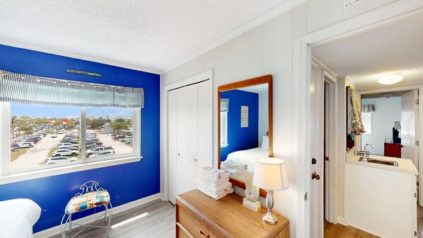 Habitación de hotel con un ventanal grande, una cama, un aparador de madera y un baño visible a través de una puerta abierta.