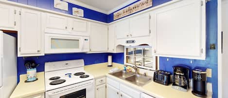 A kitchen with white cabinets, a stove, a microwave, a sink, and a coffee maker.