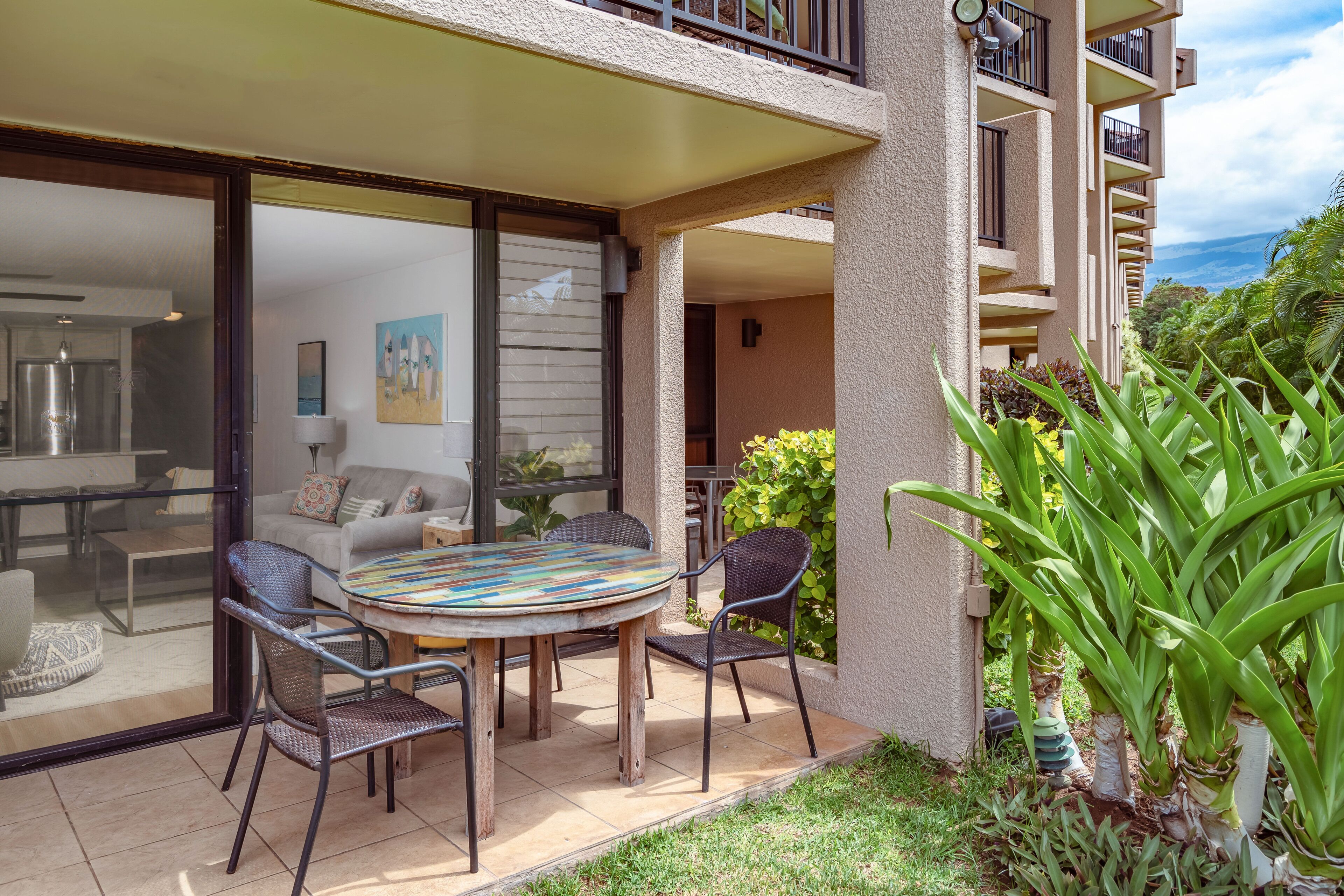 Um pátio com mesa e cadeiras redondas, porta de vidro que dá para uma sala de estar, e varanda com vista para o oceano.