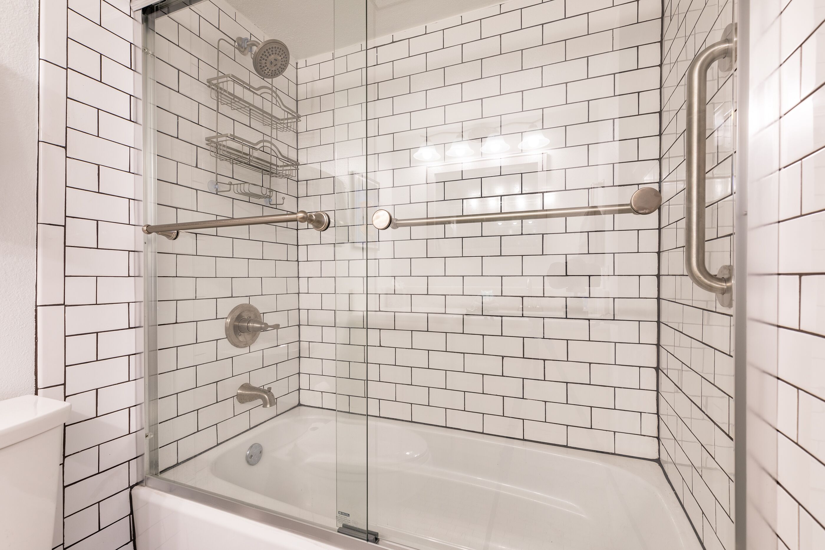 Ein modernes Badezimmer mit weißen, rechteckigen Fliesen, einer Glasdusche und einer Badewanne.