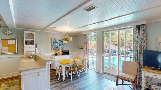 A spacious living area with a dining table, chairs, a TV, and a view of an outdoor pool.
