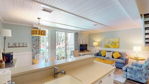 A modern kitchen with a large island, a dining area with chairs, a sofa, and a TV.