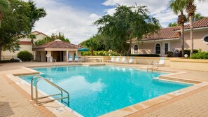 A swimming pool with clear blue water, surrounded by lounge chairs and a covered area with a palm tree. - Walk to the Beach ~ Community Pool (Miramar Beach)