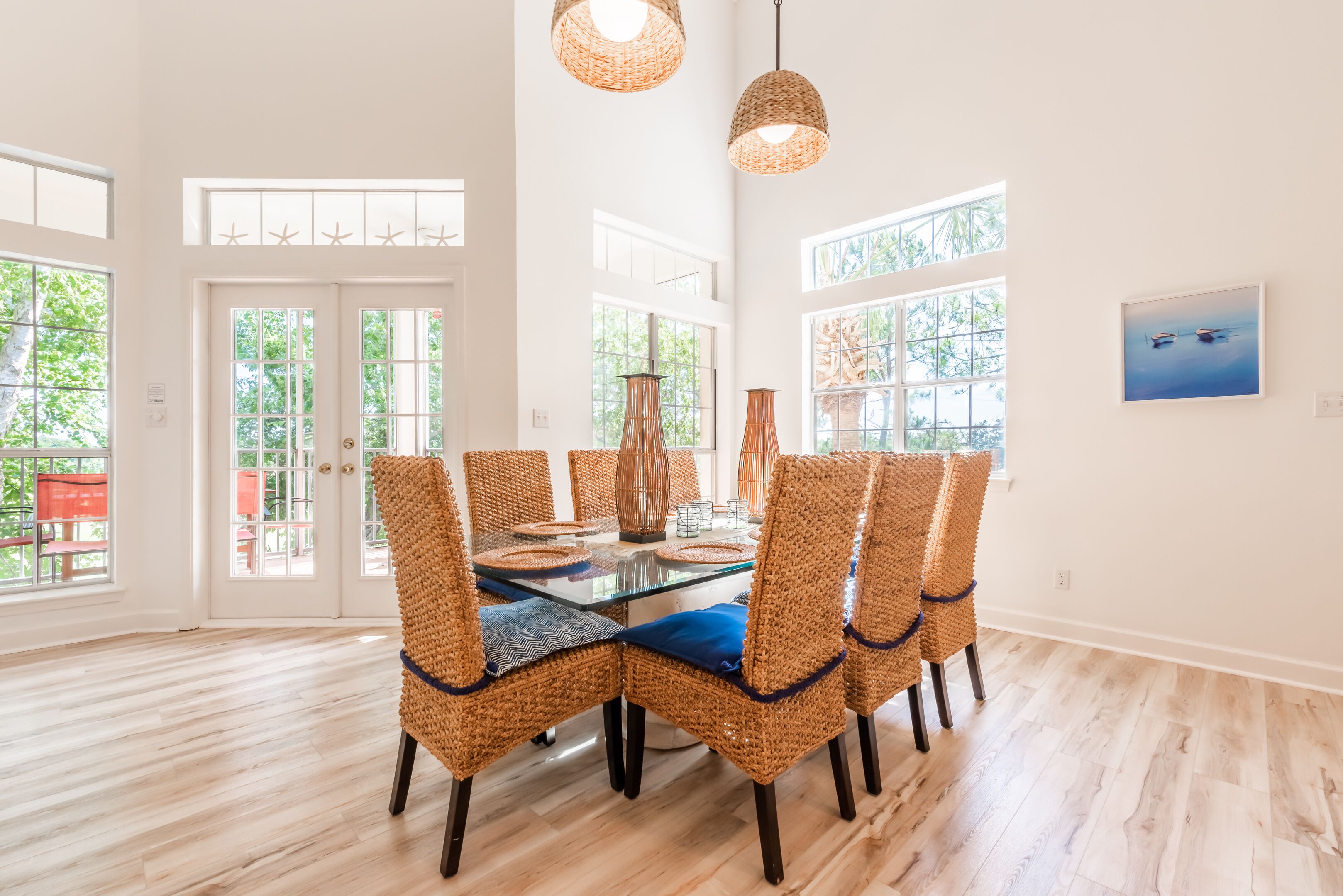 A dining area with a glass table, wicker chairs, and hanging wicker lamps.