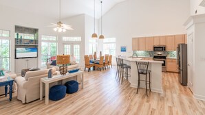 A spacious living room with a large TV, a dining area with wooden chairs, and a kitchen with wooden cabinets and a refrigerator. - Walk to the Beach ~ Community Pool (Miramar Beach)