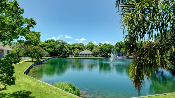 Vista deslumbrante de um lago tranquilo com uma fonte, rodeado por vegetação exuberante e um gazebo.