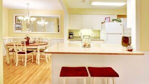 Cozinha com ilha central, armários brancos e área de jantar com mesa e cadeiras.