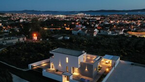 Ein modernes Haus mit geräumiger Terrasse, einem Schwimmbad und Blick auf die Stadt im Abenddämmerung.