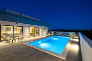A modern house with a swimming pool, outdoor seating, and a well-lit patio area. - Villa Oasis (Zadar)