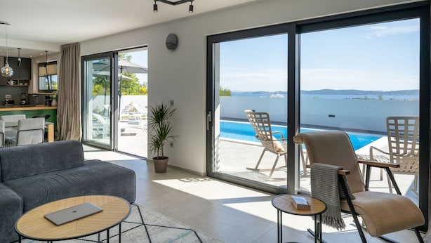 Ein modernes Wohnzimmer mit Sofa, Couchtisch und Blick auf Pool und Meer.
