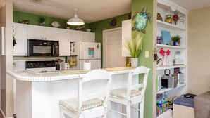 A kitchen with white cabinets, a microwave, and a refrigerator. There are two white chairs with striped cushions.
