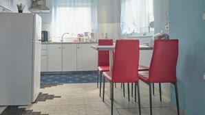 Une cuisine compacte avec des meubles blancs, un réfrigérateur en acier inoxydable et un coin repas avec des chaises rouges.