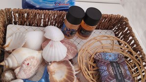 Un panier en osier contenant des coquillages, une étoile de mer bleue et deux flacons de produits essentiels pour la peau.