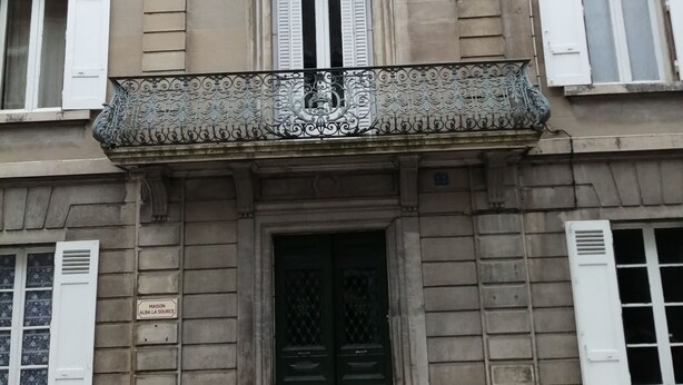 Un bâtiment doté d’une entrée centrale, de nombreuses fenêtres avec volets et d’un balcon décoratif.
